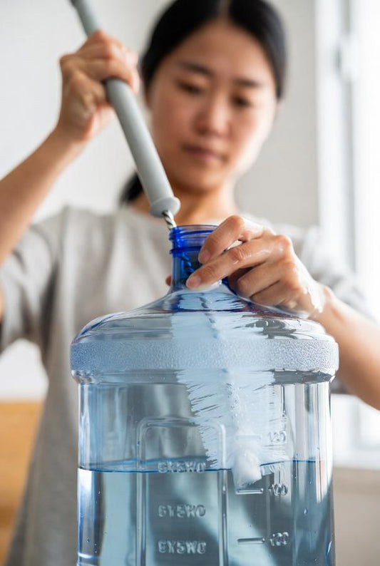 5 gallon jug being cleaned by a person the hard way with a long brush